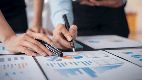 Hand writing with pen on paper sheets containing graphs and charts.