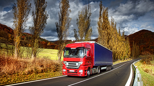 Red Semi truck driving in front of trees and mountains