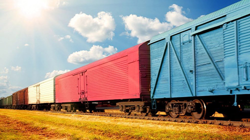 Rail carts on tracks going through grassy field with blue cloudy sky.