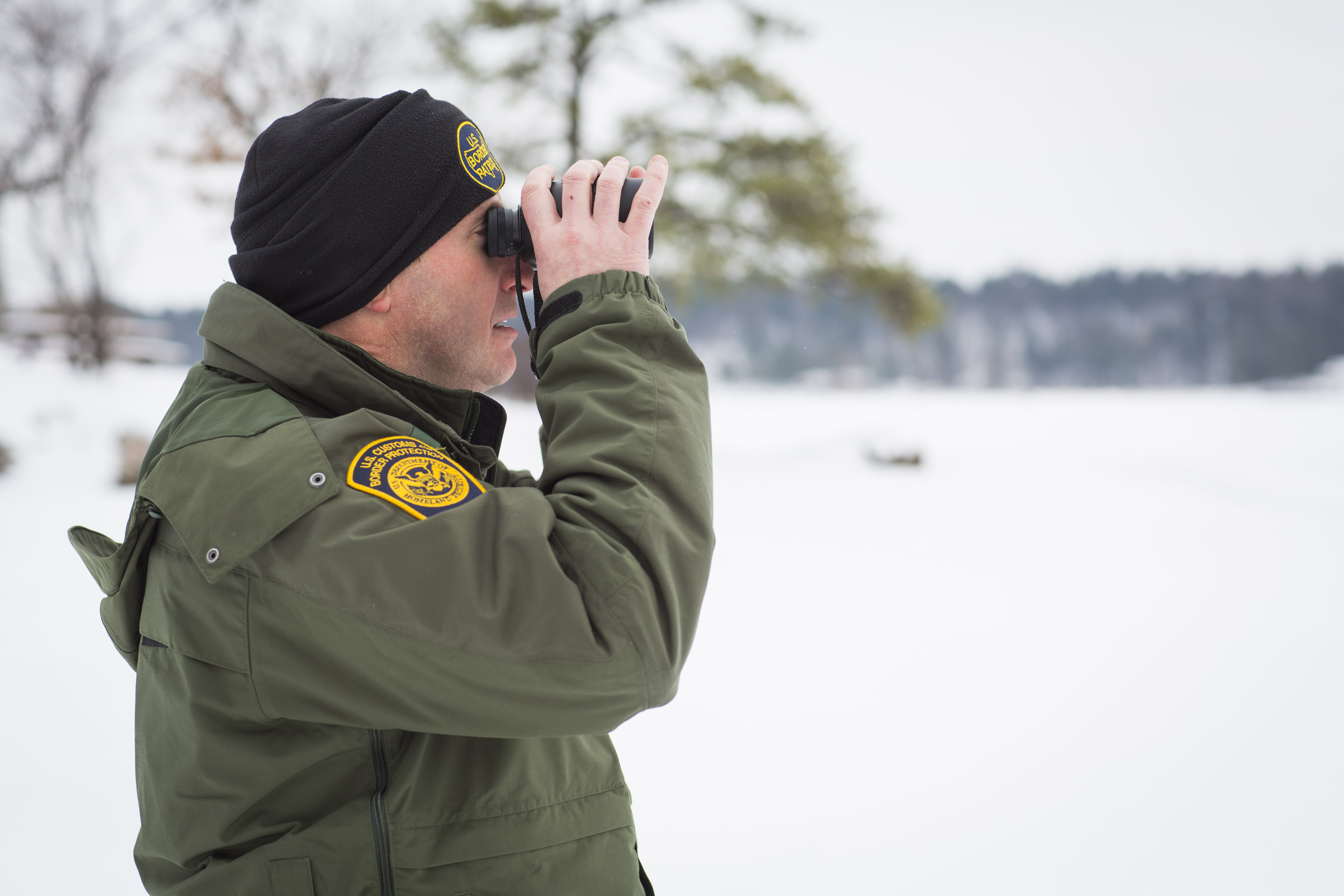Photo of a Border Patrol agent using binoculars in surveillance along the St. Lawrence River