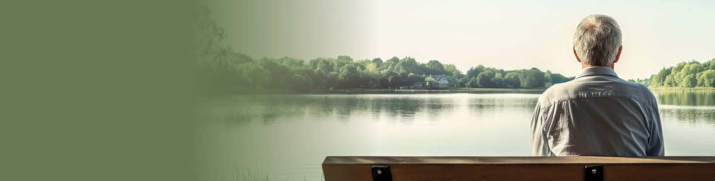 Older gentleman sitting on bench, next to the lake, looking out into the distance