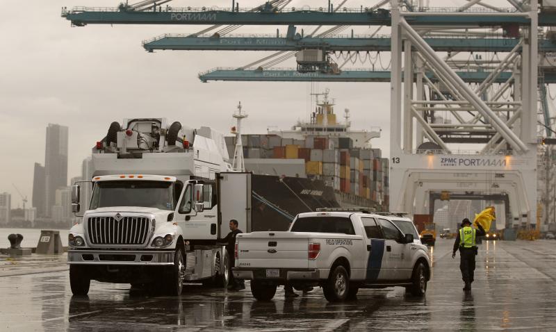 A U.S. Customs and Border Protection officer, right, shakes off his rain coat as he and a fellow officer wrap up scanning of shipping containers as they inspect incoming cargo at the Port of Miami.