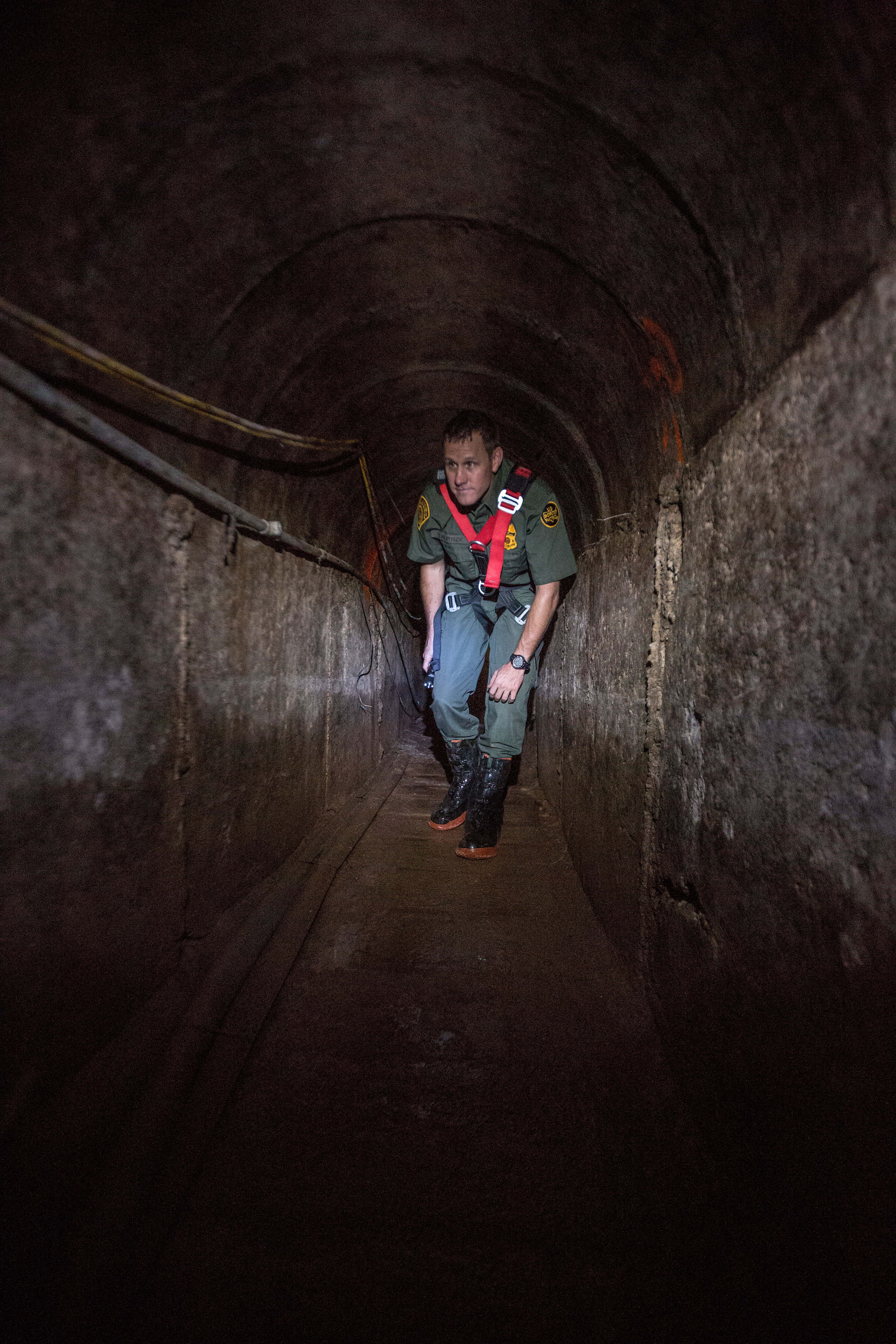Border Patrol agent kneels as he investigates tunnel.