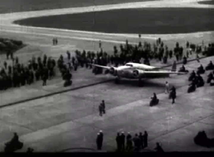 Hughes' plane landing at Floyd Bennett Field on its final touchdown for the round the world record, with the crowds on either side of the runway.