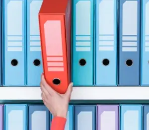 Image of binders on shelf with hand pulling one binder off the shelf