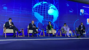 Five people are seated on a stage in front of a screen displaying a globe