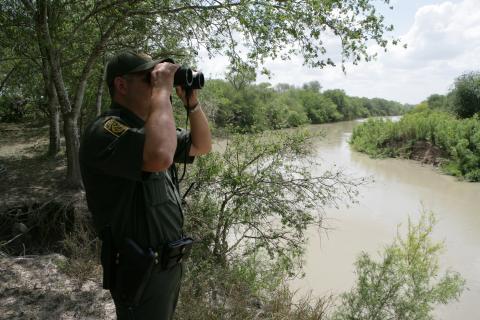 U.S. Border Patrol agent scans the area into Mexico with binoculars looking for illegal immigrants potentially staging to enter 