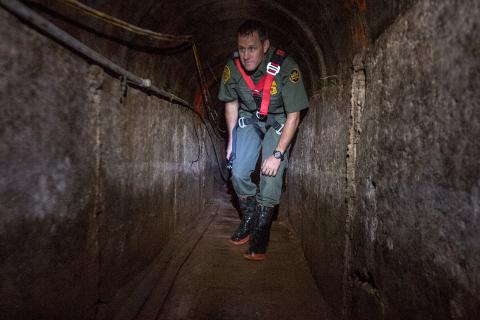 Border Patrol agent kneels as he investigates tunnel.