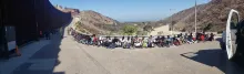 A group of migrants sit along side the road near border wall