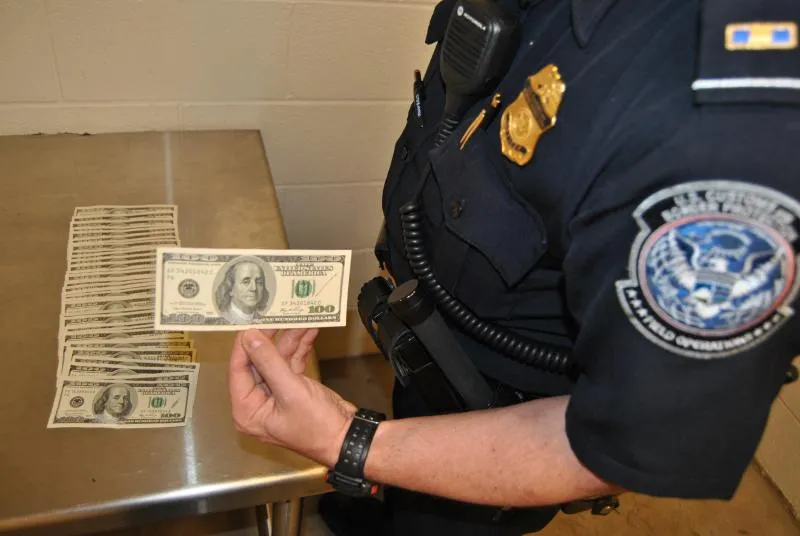 A CBP officer holds one of 37 counterfeit $100 bills seized at DFW on Monday