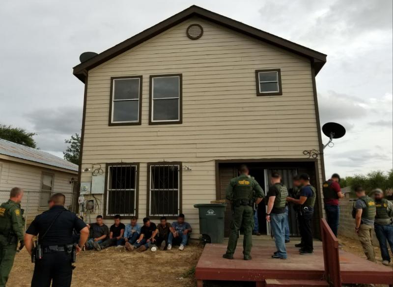 stash house with illegal aliens sitting down in front with BP agents standing in front of them as well as to the side