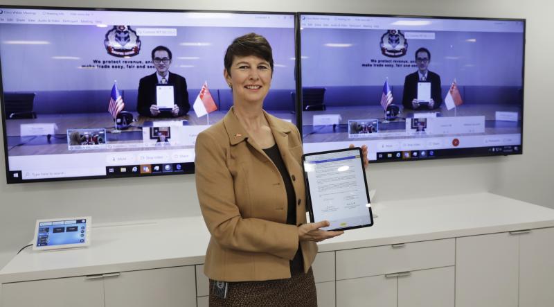 CBP Executive Assistant Commissioner Brenda Smith displays the signed letter of intent while Singapore Customs Deputy Director General Lim Teck Leong appears onscreen behind her.